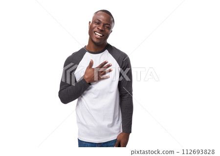 young positive african man dressed in a spring jacket holds his hand to his chest and greets 112693828