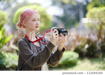 Beautiful Young artist Woman taking photo in flowers garden. Young cute girl carry the camera in the garden. 112694200