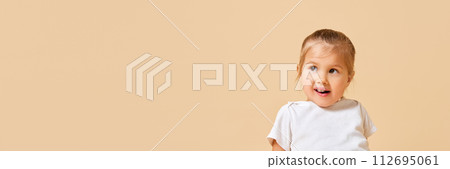 Banner. Portrait of cute, playful little girl looking away against beige studio background with negative space to insert text. 112695061