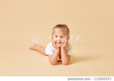 Portrait of charming pretty child, cute little girl put her head on hands against pastel color background. Baby with curious expression. 112695073