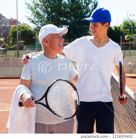 Grandfather and grandson talking on court playing tennis 112695402