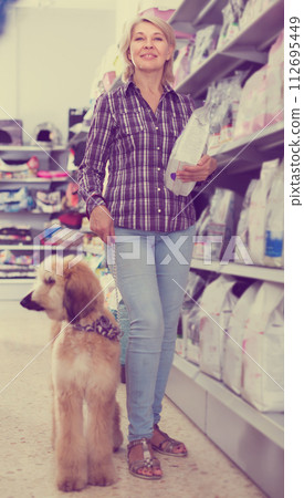 Female with Afghan Shepherd puppy choose pet food in zoo store 112695449