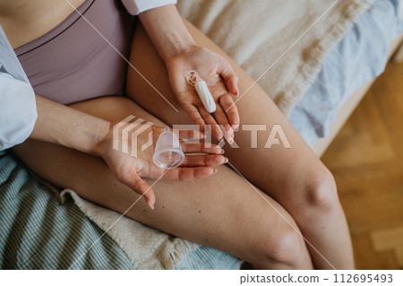 Woman holding menstrual hygiene products, period supplies. Menstrual cup and tampon in palms, close up. 112695493