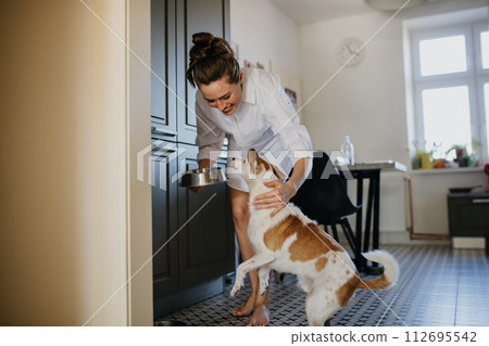 Woman in pajamas feeding dog. Weekend morning routine at home. Hygge lifestyle. Woman in pajamas feeding dog. Weekend morning routine at home. Hygge lifestyle. 112695542