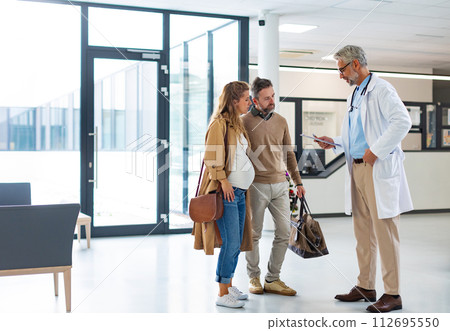 Pregnant woman and husband talking to obstetrician in hospital. Admitting woman in labor to maternity ward, planned cesarean section delivery. Pregnant woman and husband talking to obstetrician in hospital. Admitting woman in labor to maternity ward, planned cesarean section delivery. 112695550