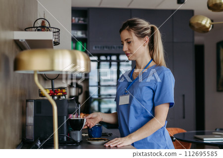 Female nurse or doctor getting ready for work in the morning, making coffee and preparing breakfast. Work-life balance for healthcare worker. 112695585