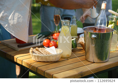 Close up shot of side table by grill at a summer garden party. Work table with wine, fresh vegetables, bread and knife. 112695624