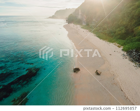 Beach with ocean, green cliffs and sunshine in Bali. Aerial view of tropical vacation coastline 112695857