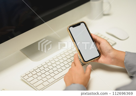 Closeup female office worker holding smartphone with empty screen sitting at her workplace 112696369