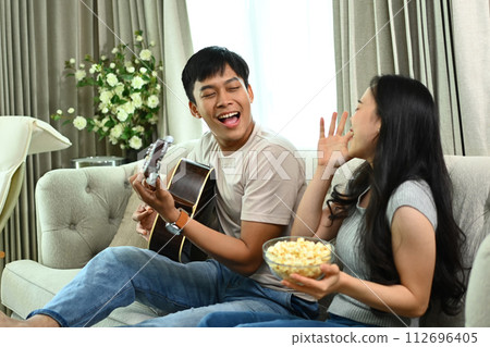 Shot of young man playing guitar for his girlfriend sitting on couch at home 112696405