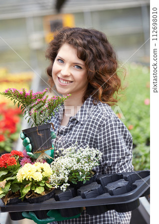 happy female nursery worker trimming plants in greenhouse 112698010