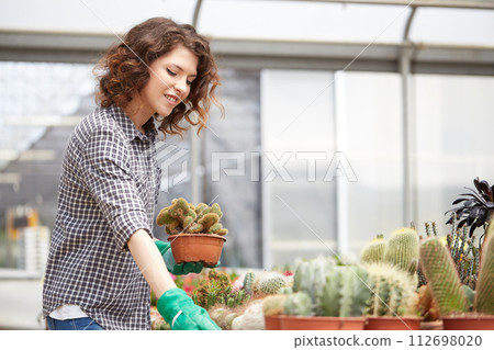 happy female nursery worker trimming plants in greenhouse happy female nursery worker trimming plants in greenhouse 112698020
