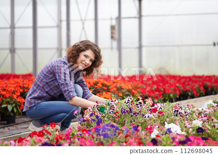 happy female nursery worker trimming plants in greenhouse 112698045