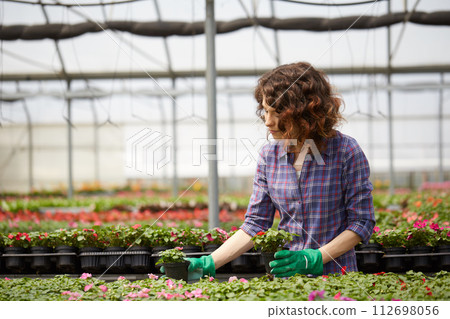 happy female nursery worker trimming plants in greenhouse 112698056
