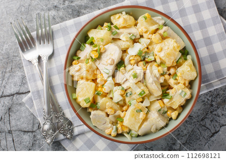 Chicken pineapple salad with corn, cheese, eggs and onions dressed with mayonnaise close-up in a plate. Horizontal top view 112698121