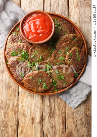 Fried beef liver patties served with tomato sauce and herbs close-up in a plate on the table. Vertical top view Fried beef liver patties served with tomato sauce and herbs close-up in a plate on the table. Vertical top view 112698134