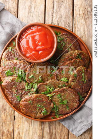 Delicious beef liver patties served with tomato sauce close-up in a plate. Vertical top view Delicious beef liver patties served with tomato sauce close-up in a plate. Vertical top view 112698135