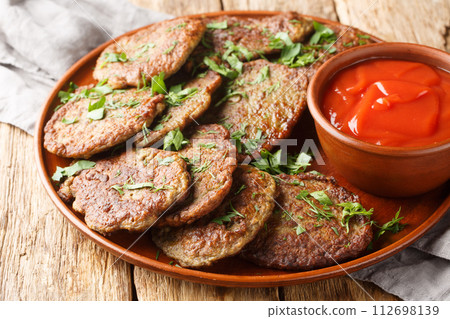 Spicy liver pancakes served with tomato sauce and herbs close-up in a plate. Horizontal Spicy liver pancakes served with tomato sauce and herbs close-up in a plate. Horizontal 112698139
