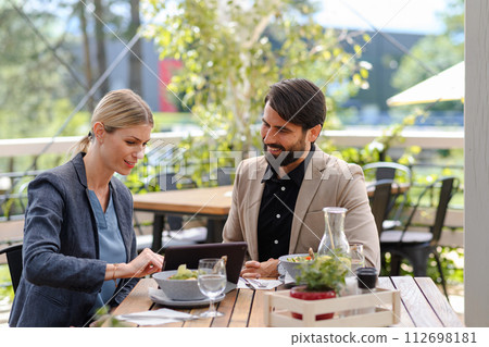 Business lunch for two managers, discussing new business project. Couple sitting outdoors on terrace restaurant, having dinner date. 112698181