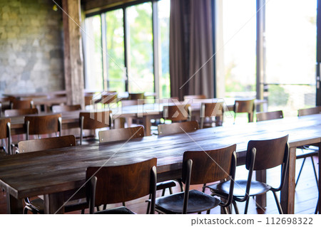 Modern restaurant with long wooden tables, chairs, and flooring. Ambient atmosphere, rustic interior design. Modern restaurant with long wooden tables, chairs, and flooring. Ambient atmosphere, rustic interior design. 112698322