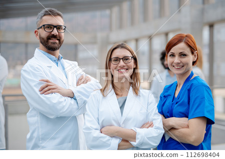 Portrait of three doctors, looking at camera, smiling. Healthcare team in medical uniforms in hospital. Portrait of three doctors, looking at camera, smiling. Healthcare team in medical uniforms in hospital. 112698404