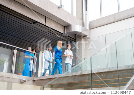 Team of doctors walking across hospital corridor. Colleagues, doctors team discussing medical case. Team of doctors walking across hospital corridor. Colleagues, doctors team discussing medical case. 112698447