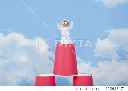 a white astronaut figurine with gold helmet on a pyramid of red paper cups 112698471