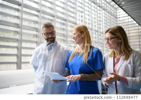 Team of doctors discussing test results, walking across corridor. Colleagues discussing patients diagnosis. 112698477
