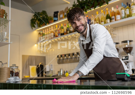 Handsome man bartender wiping bar counter in coffee house Handsome man bartender wiping bar counter in coffee house 112698596