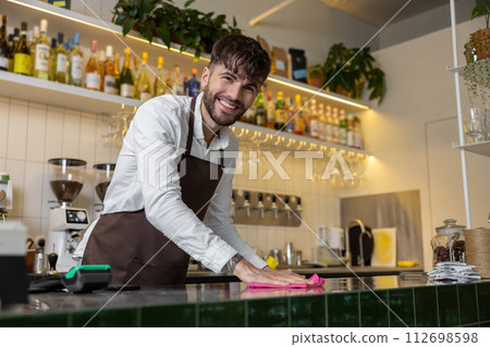 Male barista wiping bar counter at work in cafe Male barista wiping bar counter at work in cafe 112698598