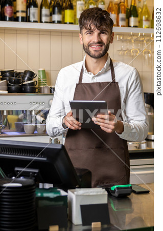 Man or waiter in apron with tablet pc computer at bar or coffee shop Man or waiter in apron with tablet pc computer at bar or coffee shop 112698632