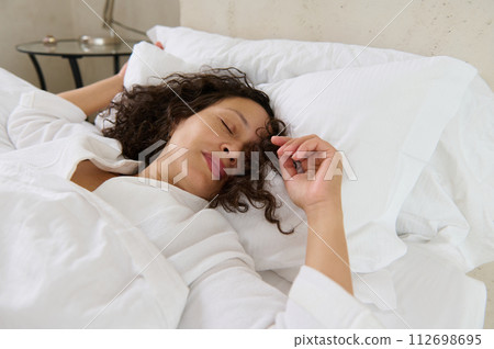 Relaxed young woman sleeping in her bed covered with white soft blanket. Woman napping in the morning. Its time to we up 112698695