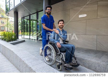 Young dark-haired male nurse taking a patient in wheelchair for walk 112698759