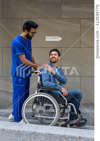 Dark-haired male nurse taking a patient in wheelchair for a walk 112698778