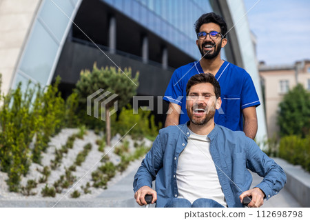 Dark-haired male nurse taking a patient in wheelchair for a walk 112698798