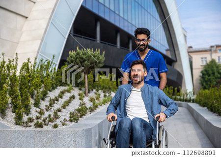 Dark-haired male nurse taking a patient in wheelchair for a walk 112698801