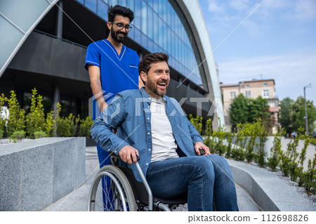 Young smiling bearded man in wheelchair having a walk with a nurse Young smiling bearded man in wheelchair having a walk with a nurse 112698826