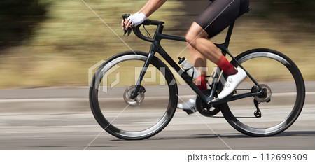 Motion blur of a bike race with the bicycle and rider at high speed. Professional male cyclist in racing outfit during a ride on bike outdoors. Panning technique used Motion blur of a bike race with the bicycle and rider at high speed. Professional male cyclist in racing outfit during a ride on bike outdoors. Panning technique used 112699309