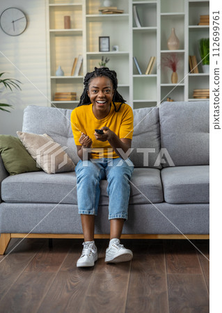 Young african american woman sitting on the sofa at home Young african american woman sitting on the sofa at home 112699761