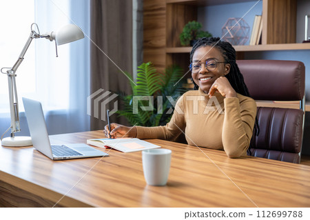 Cheerful woman with dreadlocks works remotely using laptop and technology Cheerful woman with dreadlocks works remotely using laptop and technology 112699788