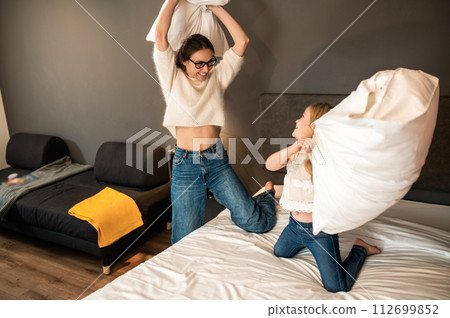 Mother and her little daughter playing with cushions on bed in hotel room Mother and her little daughter playing with cushions on bed in hotel room 112699852