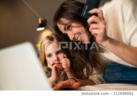 Mother and daughter booking vacation together using laptop and credit card online shopping 112699892