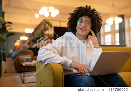 Young curly-haired man with laptop working in a hotel hall 112700013