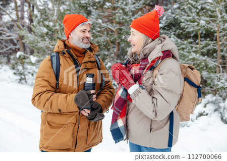 Smiling mature couple having hot tea in a winter forest Smiling mature couple having hot tea in a winter forest 112700066