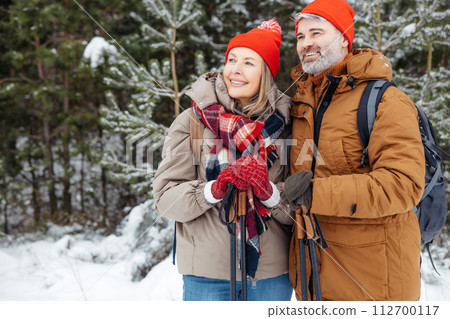 Mature man and woman standing in a winter forest and looking contented 112700117