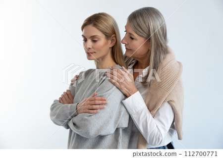 Gray-haired good-looking woman hugging her daughter with tenderness Gray-haired good-looking woman hugging her daughter with tenderness 112700771