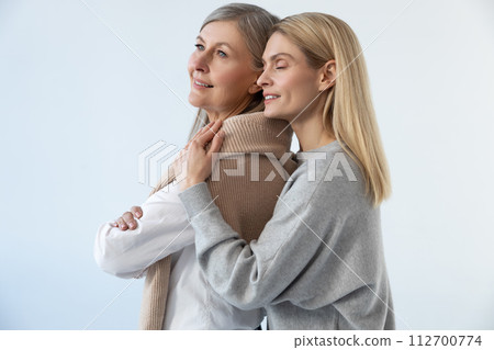 Blonde young woman hugging her mom and looking peaceful Blonde young woman hugging her mom and looking peaceful 112700774