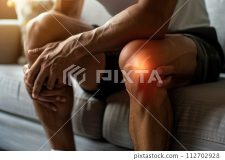 Man sitting on a couch and holding his knee. he having knee pain. Generative AI 112702928