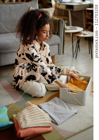 Full length portrait of young woman folding and sorting clean clothes on laundry day 112703208