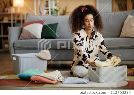 Portrait of young African American woman folding and putting away clean clothes while cleaning home on weekend Portrait of young African American woman folding and putting away clean clothes while cleaning home on weekend 112703224